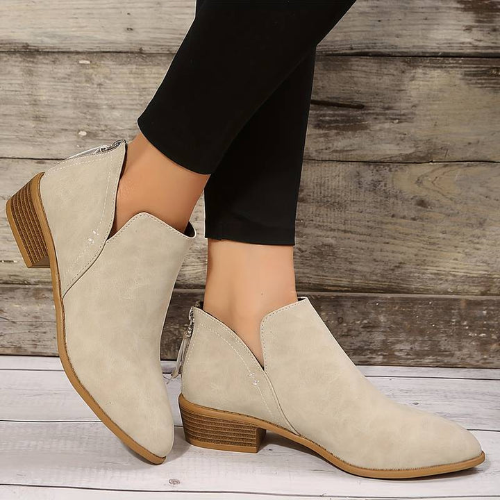 Beige ankle boots with brown soles worn by a person against a wooden background